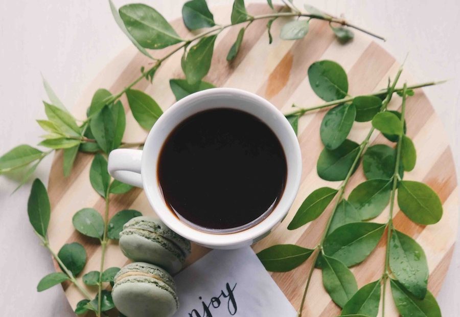 Xicara de cafe com creatina em uma mesa com umas plantas do lado