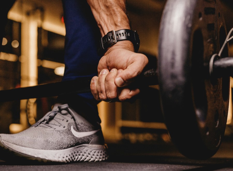 Mão de uma homem fazendo deadlift em uma barra na academia